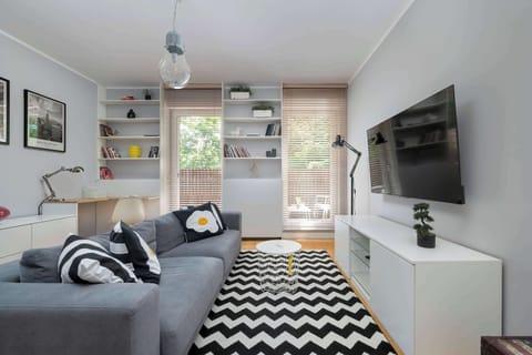 A spacious and bright living room with a large window, a comfortable sofa, and a modern wall-mounted TV creates the perfect space for relaxation.