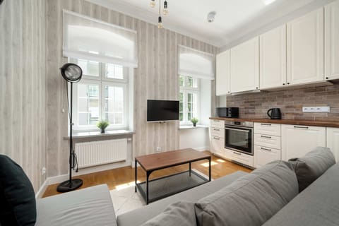 A cozy living room with a sectional sofa, wooden floor, and large windows filling the space with natural light, seamlessly connected to a modern kitchen area.