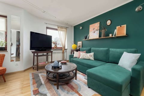 Living room with a green corner sofa, TV, coffee table, and a cozy, stylish vibe.
