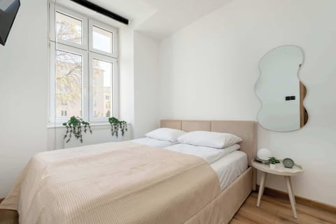 A bright bedroom with a large window and a decorative mirror offers a pleasant space to relax.