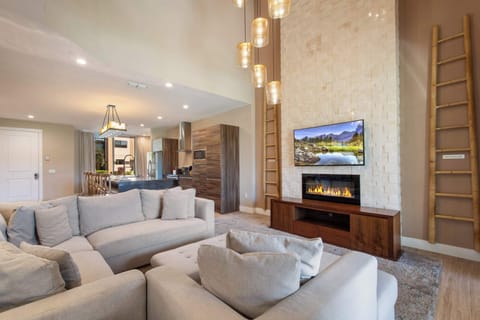 Bright open living room with cozy sectional, stone fireplace, and modern kitchen view.
