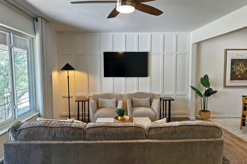 Bright and cozy living room with large windows, stylish paneling, and a mounted smart TV.