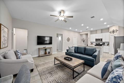 Spacious open-concept living room with comfy seating, a 65″ Smart TV, and easy flow to the kitchen.
