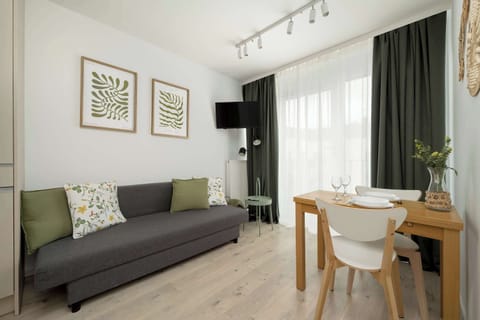 A modern living area where the grey sofa and wooden table take centre stage. A flat-screen TV hangs on the wall.na część dzienna gdzie główną rolę odgrywa szara sofa i drewniany stół. Na ścianie zawieszony jest telewizor z płaskim ekranem.