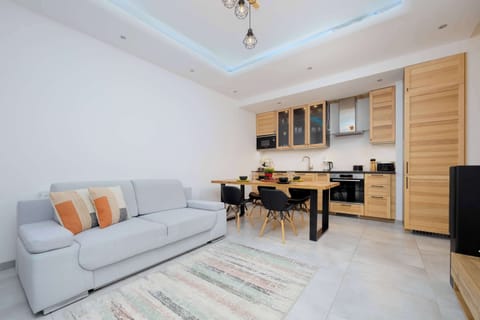 A spacious living room with a grey sectional sofa and a coffee table. In the background, there’s a small dining area with chairs.