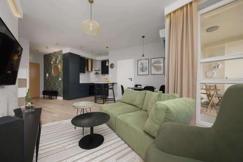 A stylish open-plan living room and kitchen with a green sofa and modern bar stools. The layout creates a spacious and sociable environment.