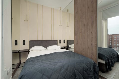 A cozy bedroom with a large bed framed by modern cabinetry and a floor-to-ceiling window letting in natural light.