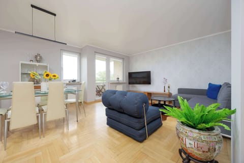 A bright living and dining area with a blue sofa set, wooden floors, and a table set for four under natural daylight.