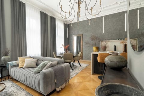 A living room with a stylish gray and beige color scheme, a chandelier, and a cozy seating area with a round dining table and plush chairs.