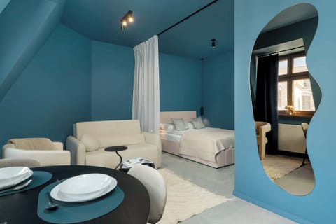 A compact dining area with a round table and two chairs, positioned near a soft seating space and under slanted ceilings painted in bold blue.
