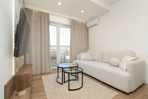 Bright and beige living room with television, coffee tables, and double sofa bed.