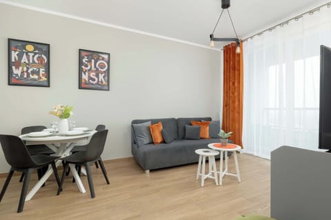A bright and cosy living room with a grey sofa. The living area is harmoniously connected to the dining area with a white table with round top and black stylish chairs.