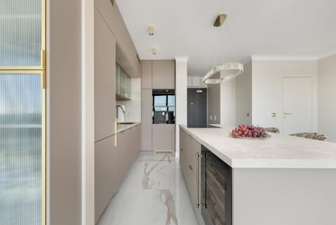 A modern kitchenette with an elegant island, marble floor and large floor-to-ceiling windows impresses with its spaciousness, natural light and stylish hockers with upholstered seats and golden legs, creating a luxurious space ideal for cooking.