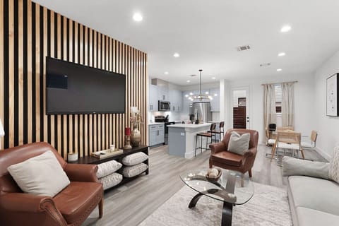 Relax in the stylish living room featuring a modern wood-accent wall, a large flat-screen TV, and comfortable seating—perfect for unwinding after exploring Houston!