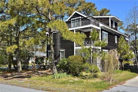 A charming angle showcases the durable construction of the home, accented by the inviting upper deck and surrounding lush landscaping of tall pines and neatly trimmed bushes.