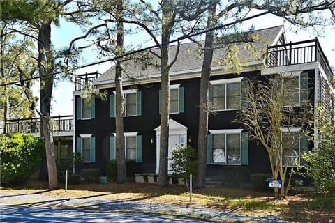 This striking two-story vacation home features a black exterior with multiple windows framed by green shutters and a welcoming front porch flanked by tall trees.