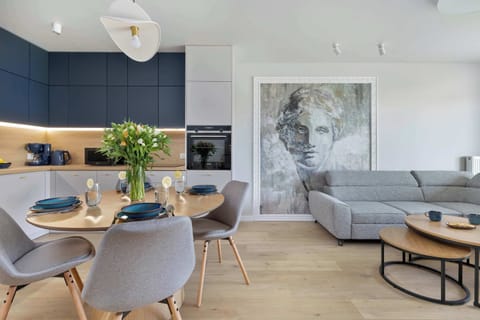 A modern living and dining area with a gray L-shaped sofa, round coffee table, and dining setup next to a bright window.