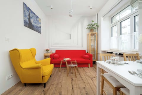 A cozy living room with a bright red sofa, yellow armchair, and white coffee table on wooden flooring.