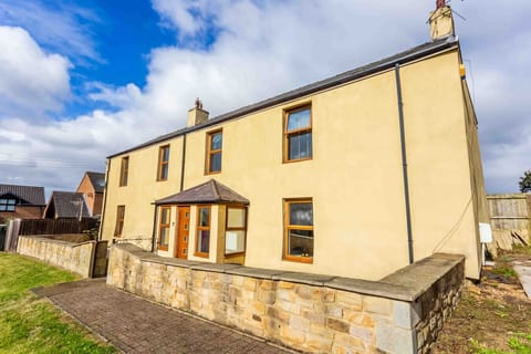 This charming two-storey home boasts a clean, modern facade with warm wooden-framed windows and a stone-accented entryway. Set behind a low stone wall, the property offers a spacious, welcoming presence in a peaceful residential setting.