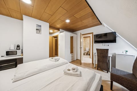 Geräumiges Zimmer mit Doppelbett, TV, Schreibtisch und Pantry mit Mikrowelle sowie Wasserkocher; Kleiderschrank und Zugang zum Bad runden die Ausstattung ab.


