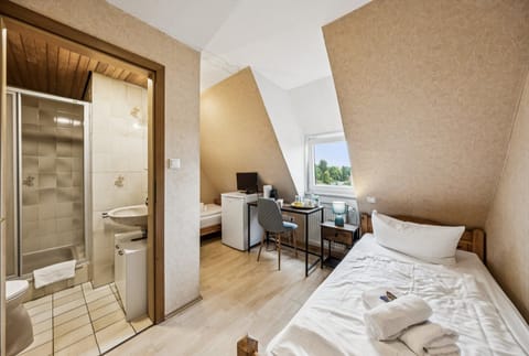 Einzelzimmer mit eigenem Bad nebenan, Arbeitsbereich, Minikühlschrank und Kaffeestation – kompakt, hell und gut ausgestattet.