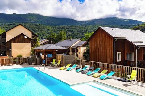 Inviting seasonal pool framed by timber chalets and panoramic Pyrenean peaks.