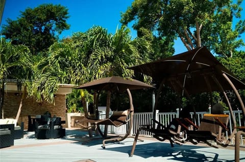 Outdoor kitchen/dining space with sofas, table, and shaded swinging chairs.
