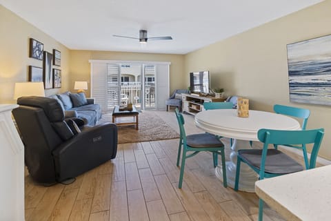 Relax in this inviting beachside condo featuring a cozy living room, vibrant dining area, and sliding doors leading to a balcony with refreshing coastal breezes.
