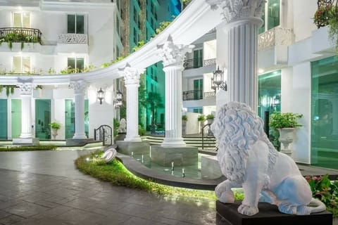 Entrée somptueuse avec colonnes classiques et statue de lion en pierre, symbolisant force et élégance. Fontaines et éclairage subtil créent une ambiance prestigieuse. Un cadre luxueux pour un séjour inoubliable dans une architecture inspirée!