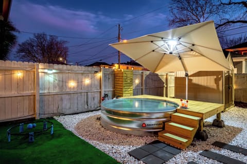 Unwind in style under the stars ✨ This cozy backyard retreat features a charming stock tank soaking tub, ambient string lights, and a shaded deck perfect for evening cocktails.