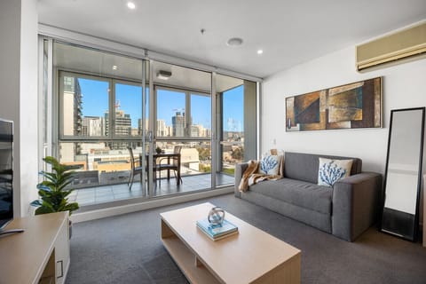 Unwind in the living area as natural light streams through floor-to-ceiling doors and the city unfolds beyond.
