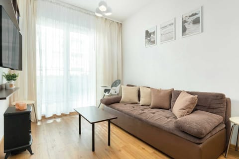 A cozy living room with a brown sofa, sheer white curtains, and a small wall-mounted TV for a relaxed atmosphere.