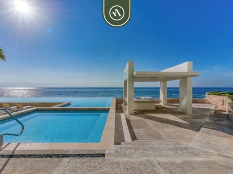 Oceanfront swimming pool area complete with a white concrete shade structure.