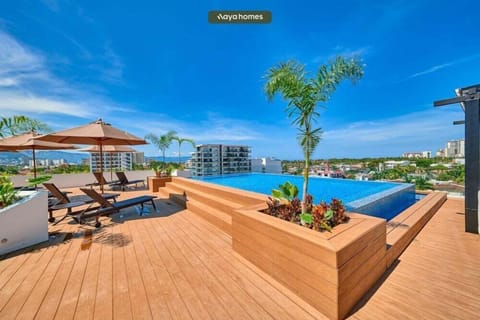 Sunny terrace space featuring modern lounge chairs, umbrellas, and raised wooden planters with tropical greenery.
