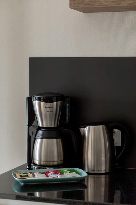 A detail shot of a coffee station with a black coffee maker. Set within a clean and modern kitchenette.
