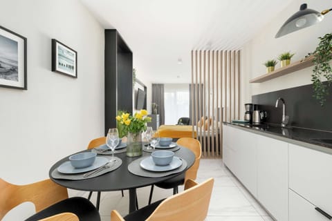 A compact kitchenette with modern white cabinetry, black countertops, and essential appliances. A round dining table with elegant chairs is placed nearby for comfortable meals.