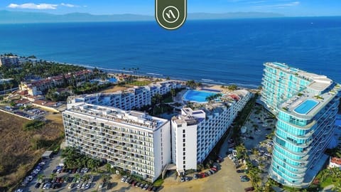 An aerial perspective of a premium apartment complex situated right on the coast, showcasing the proximity to the beach and the expansive pool deck.