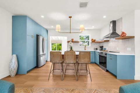 Gourmet kitchen with sleek quartz countertops, custom blue cabinetry, brass accents, and high-end stainless steel appliances. Features an oversized island with seating, open shelving, and designer lighting—perfect for both cooking and entertaining in style