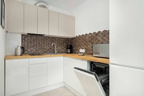 Nowoczesna kuchnia z drewnianym blatem i białymi szafkami została wyposażona w sprzęty AGD wysokiej jakości.