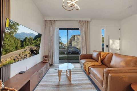 This cozy living area features a warm brown leather sofa perfect for relaxation, paired with a stylish wooden media console. Large glass sliding doors flood the space with natural light and showcase beautiful outdoor views.
