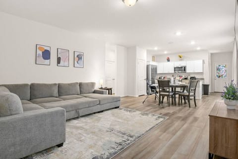 Open-concept living space featuring a spacious sectional, sleek dining area, and a bright kitchen with white cabinetry and stainless steel appliances. Stylish and functional, perfect for modern living and entertaining.