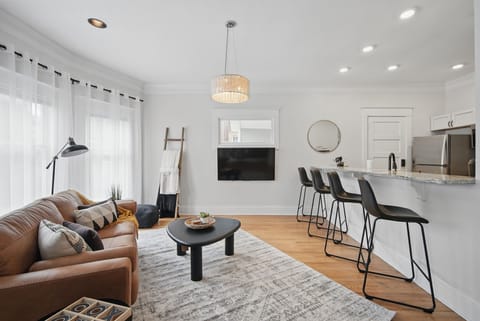 Bright and inviting living space featuring a modern leather sofa, wall-mounted smart TV, and playful textures—ideal for relaxing after a day out.