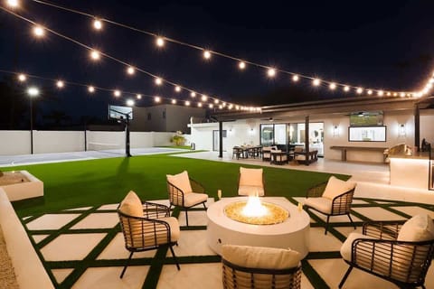 Outdoor oasis featuring a sparkling, heated optional pool with a safety fence. Multiple seating areas, lounge chairs, string lights, BBQ grill, firepit, shuffleboard, and outdoor smart TV.
