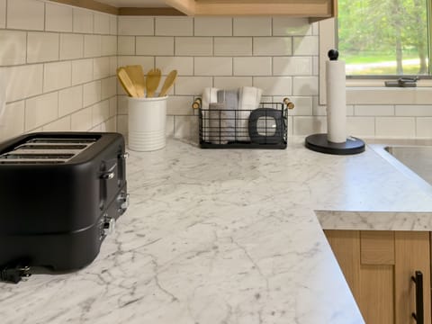 The modern kitchen countertop showcases a sleek black toaster and wooden utensils against a backdrop of elegant white tiles.
