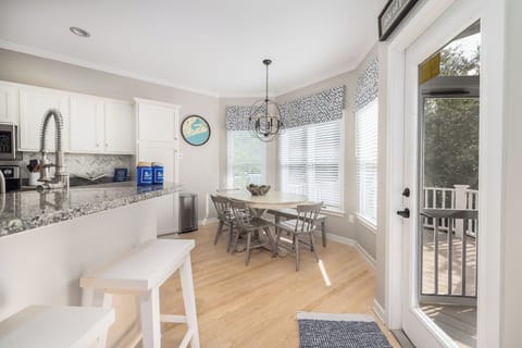 Sunlit breakfast nook with bay windows, seating for six, and chic coastal chandelier