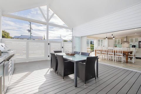 Enjoy relaxed alfresco meals on the expansive covered deck, where a six-seater dining table sits beside a full outdoor kitchen complete with built-in BBQ, sink, and generous counter space.