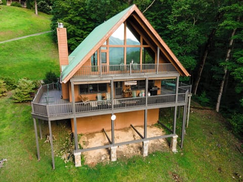 This classic A-frame rental cabin in Bryson City features two large covered decks, a green metal roof, and rustic wood siding, all surrounded by lush forest and open green space—perfect for your next mountain getaway.