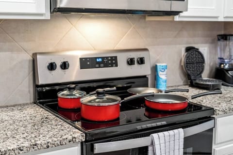 Fully equipped kitchen w modern appliances and red cookware, perfect for preparing meals. Includes extras like waffle maker for added convenience. Ideal for long-term guests who enjoy cooking and want comfort of a home-cooked meal during their stay.