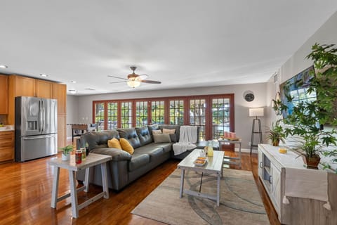 This open-concept living room welcomes you with floor-to-ceiling French doors that flood the space with natural light. The sleek leather sectional, soft gray tones, and pops of yellow accents create a cozy yet modern retreat.