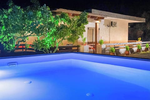 Sparkling Outdoor Pool Illuminated at Night – Large, crystal-clear swimming pool surrounded by lush greenery, softly lit for a magical evening atmosphere, perfect for a refreshing night swim or relaxing with a drink under the stars.